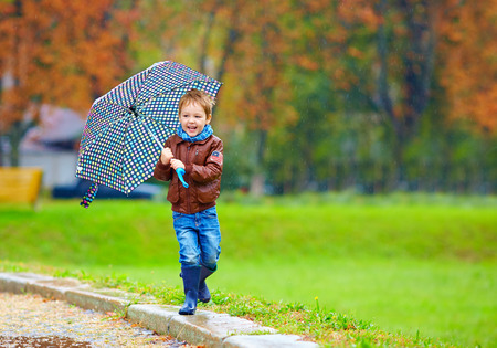 happy boy running under an autumn rainの写真素材