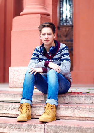 stylish teenage boy with headphones, sitting on stairsの写真素材