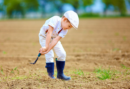 Cute little farmer working with spud on spring fieldの写真素材