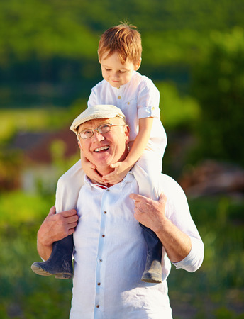 happy grandson sitting on shoulders of grandpa countrysideの写真素材