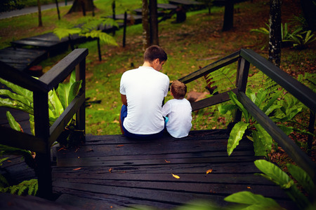 father and son sitting on wooden stairs in rain forestの写真素材