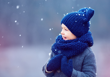 cute kid, boy in winter clothes playing under the snowの写真素材