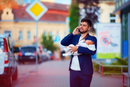 young adult businessman walking through the city with newborn baby on handsの写真素材