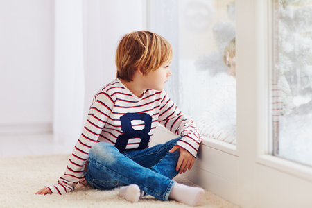 handsome young boy sitting on carpet near the window at rainy dayの写真素材