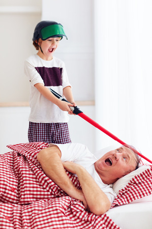 naughty yelling grandson waking grandpa up by playing around in loud, noisy gamesの写真素材