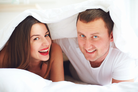 happy couple playing under duvet cover at bedroomの写真素材