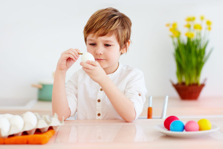 cute kid painting easter eggs at the kitchen desk