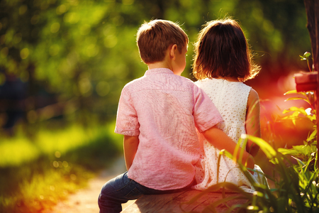 cute kids sitting together on bench in sunny spring gardenの写真素材