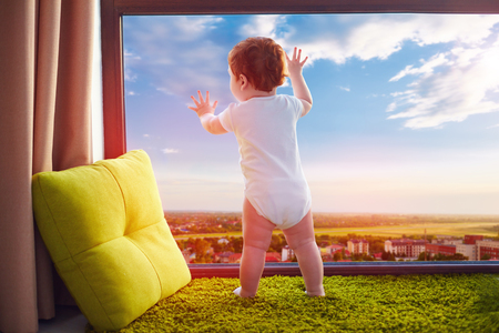 infant baby watching the beautiful valley cityscape through the window at homeの写真素材