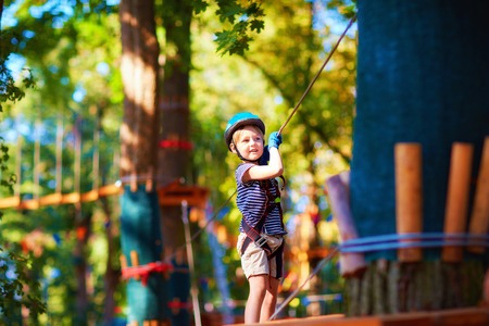 young boy passing the cable route high among the trees, extreme sport in adventure parkの写真素材