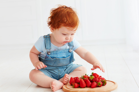 cute ginger toddler baby tasting strawberriesの写真素材