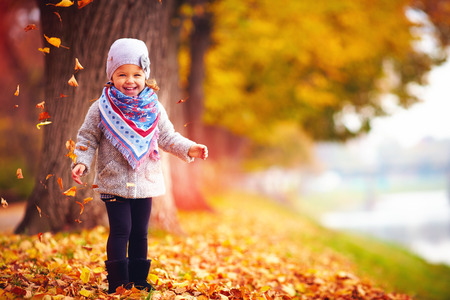 adorable happy girl playing with fallen leaves in autumn parkの写真素材