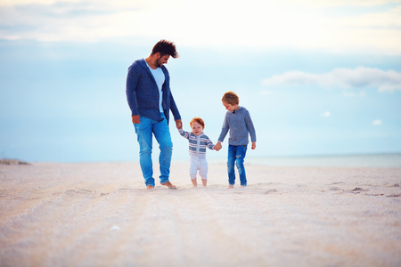 happy father and sons walking on sandy autumn beach near the seaの写真素材