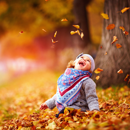 adorable happy baby girl catching the fallen leaves, playing in the autumn parkの写真素材