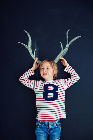 funny kid, boy with drawn antlers standing in front of a chalk wallの写真素材