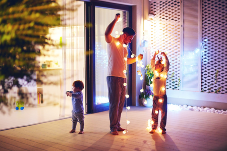 happy family, father with sons decorate open space patio area with christmas garlandsの写真素材