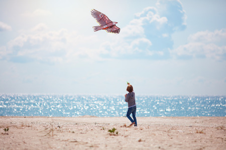 young kid, boy flying kite at sunny summer day near the seasideの写真素材