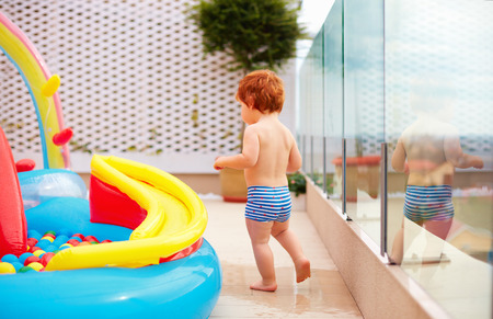 redhead baby boy having fun running around inflatable kid pool at the patioの写真素材
