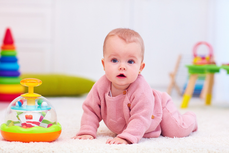 cute little baby girl crawling on the carpet among the development toysの写真素材