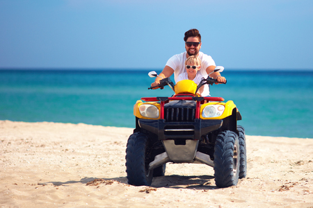 happy family, father and son riding on atv quad bike at sandy beachの写真素材