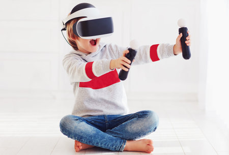 excited young boy, kid wearing virtual reality goggles, playing in video game