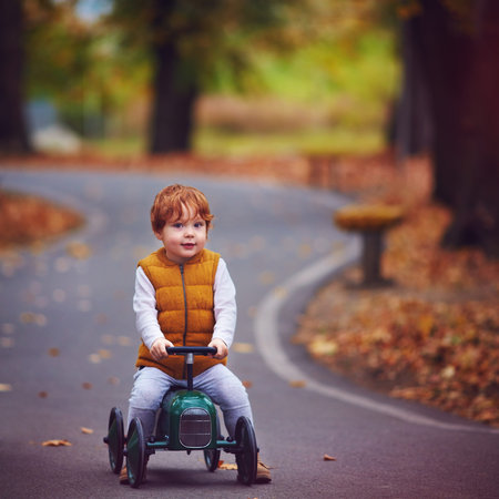 cute redhead baby boy driving a push car in autumn park