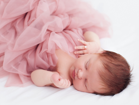 newborn, two weeks old baby girl in ruffle dress and with finger ring is sleeping peacefullyの写真素材