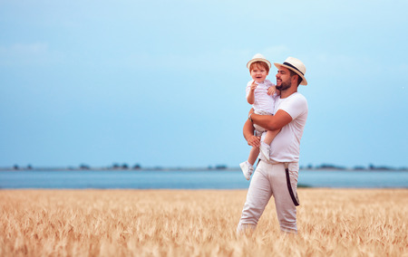 happy father with toddler son walking through the ripe wheat fieldの写真素材