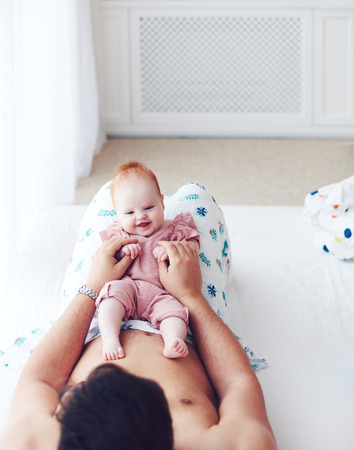young father playing with cute infant baby daughter in bed, at homeの写真素材