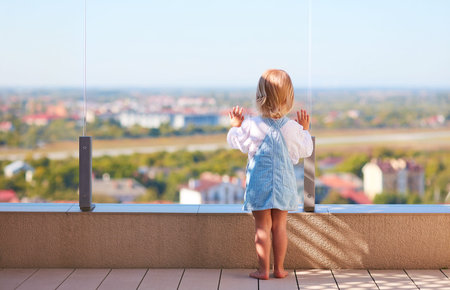 cute toddler baby girl looking on the city scape through the glass balustade at rooftop patioの写真素材