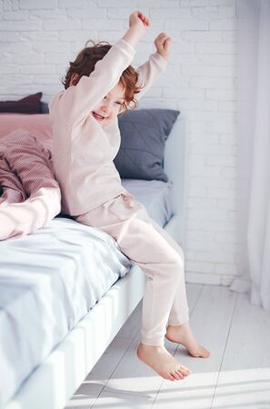 cheerful redhead baby boy getting up in the morning at sunny bedroomの写真素材
