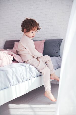 cute redhead baby boy getting up in the morning at sunny bedroomの写真素材