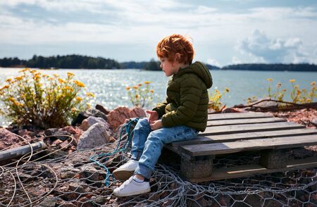 cute redhead kid sitting on wooden pallet in front of the Baltic sea and tansy flowersの写真素材