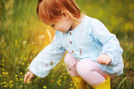 beautiful happy baby girl cropping the meadow flowers in the gardenの写真素材