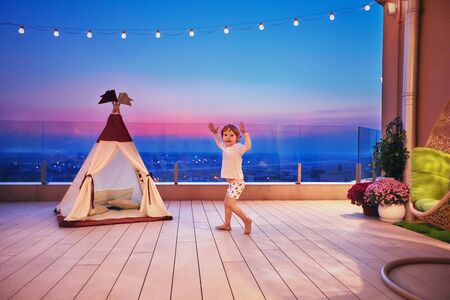 happy baby boy running all over the rooftop patio on the sunset, playing in teepee tent houseの写真素材