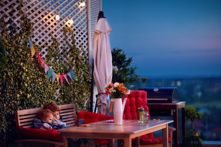 cute siblings having fun, watching cartoons on the phone, spending time on cozy rooftop patio in summer eveningの写真素材