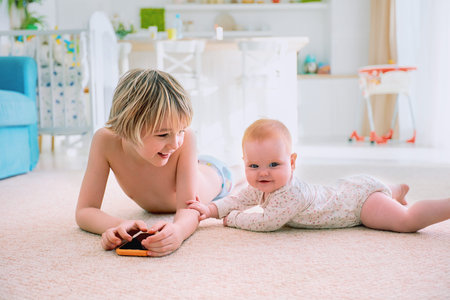 happy infant baby girl playing with elder brother on the carpet at home