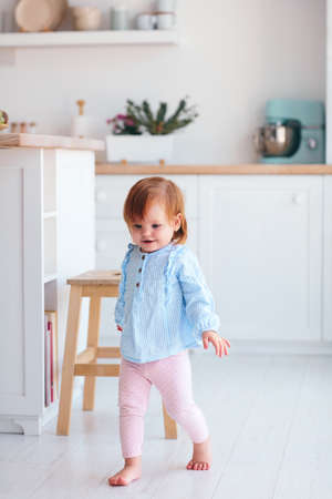 cute happy infant baby girl walking on the kitchen at homeの写真素材