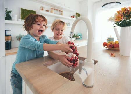 happy kids washing cherries under tap water at the kitchenの写真素材