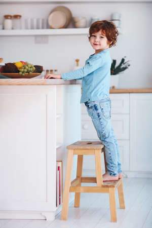 cute redhead kid, boy standing on step stool in the kitchenの写真素材