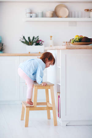 funny infant baby girl climbing a step stool at the cozy kitchen at homeの写真素材