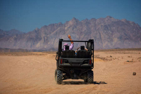 excited tourists driving away for buggy safari trip through the mountain desertの写真素材
