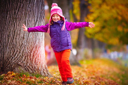 cute little girl having fun, playing with colorful leaves in autumn parkの写真素材