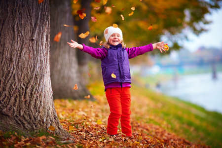 cute little girl having fun, playing with colorful leaves in autumn parkの写真素材
