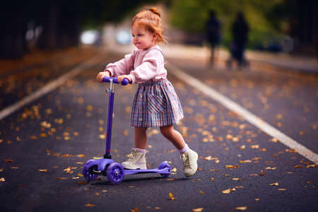 cute redhead baby girl scootering in autumn parkの写真素材