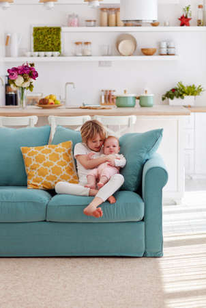 cute brother soothing sad little sister while sitting in cozy living room at homeの写真素材