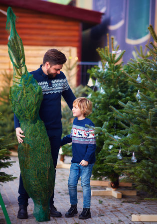 happy father and son buying a real lush christmas tree on a christmas market during winter holidaysの写真素材