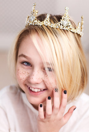 portrait of beautiful happy androgynous boy wearing crown, golden freckles and nail polish, with longe blonde hairの写真素材