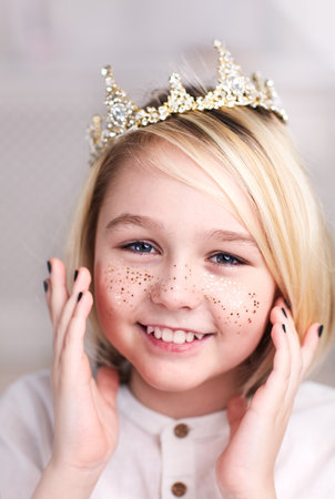 portrait of beautiful happy androgynous boy wearing tiara, golden freckles and nail polish, with long blonde hairの写真素材