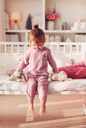 toddler baby girl sitting on the bed in sunlit nursery room at homeの写真素材